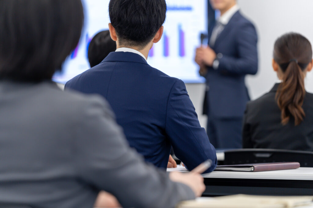 会合で登壇者の話を聞くスーツを着た人々